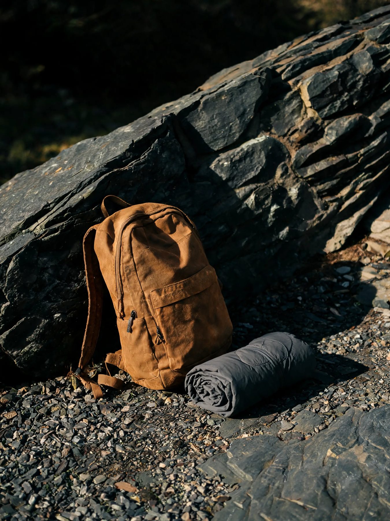 Ripstop daypack and rolled shell jacket against a slate boulder